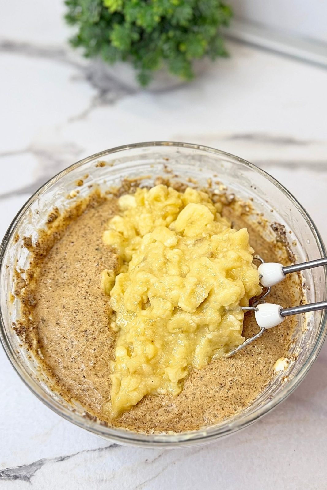 Mashed bananas added to the butter, brown sugar, and egg mixture in a glass bowl.