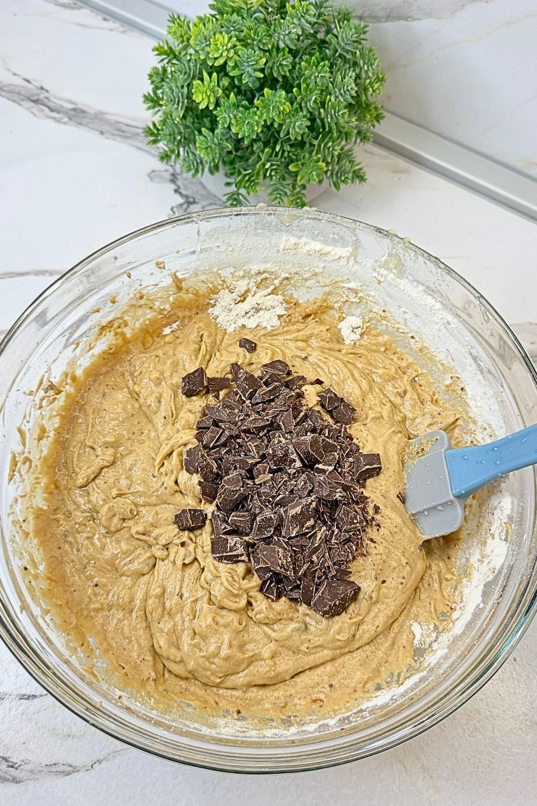 Chopped chocolate added to banana bread batter, ready to fold in with a spatula.