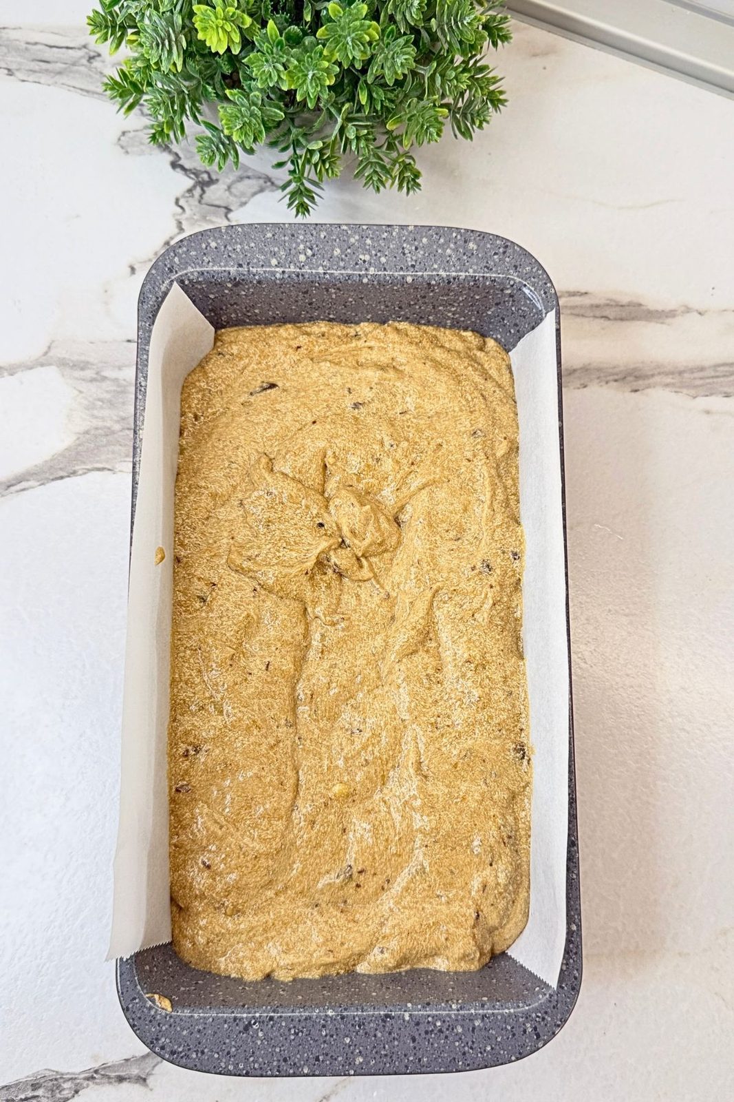 Chocolate chip banana bread batter spread evenly in a parchment-lined loaf pan.