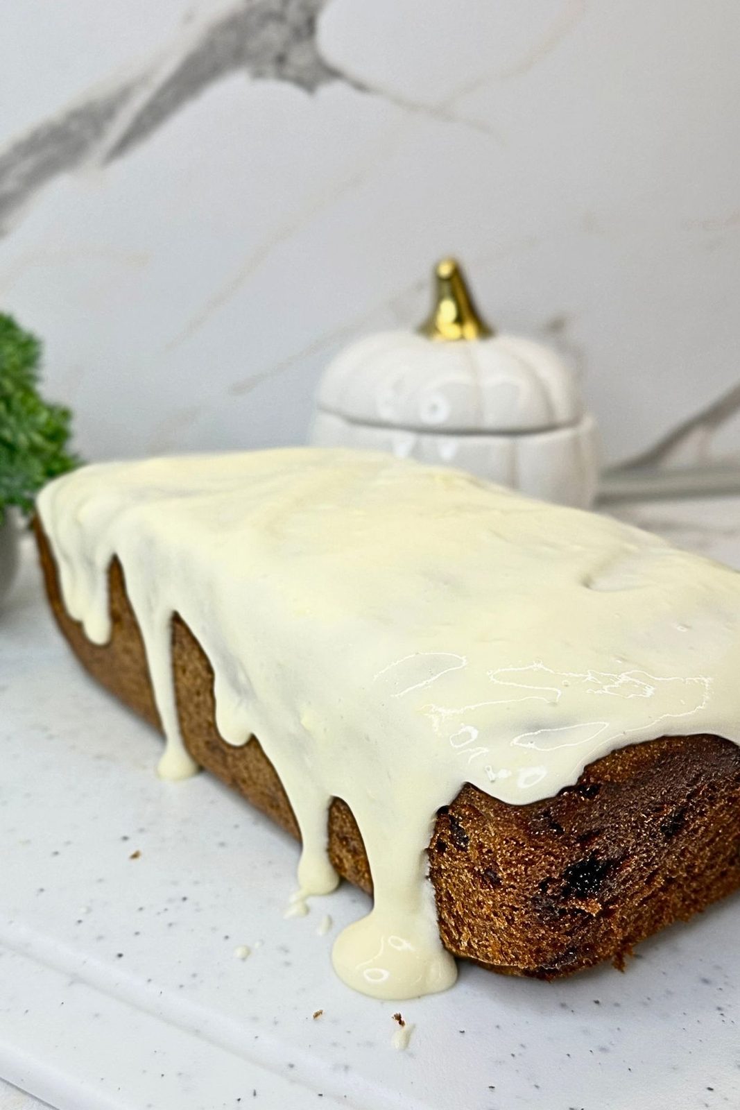Whole chocolate chip banana bread topped with cream cheese frosting dripping down the sides.