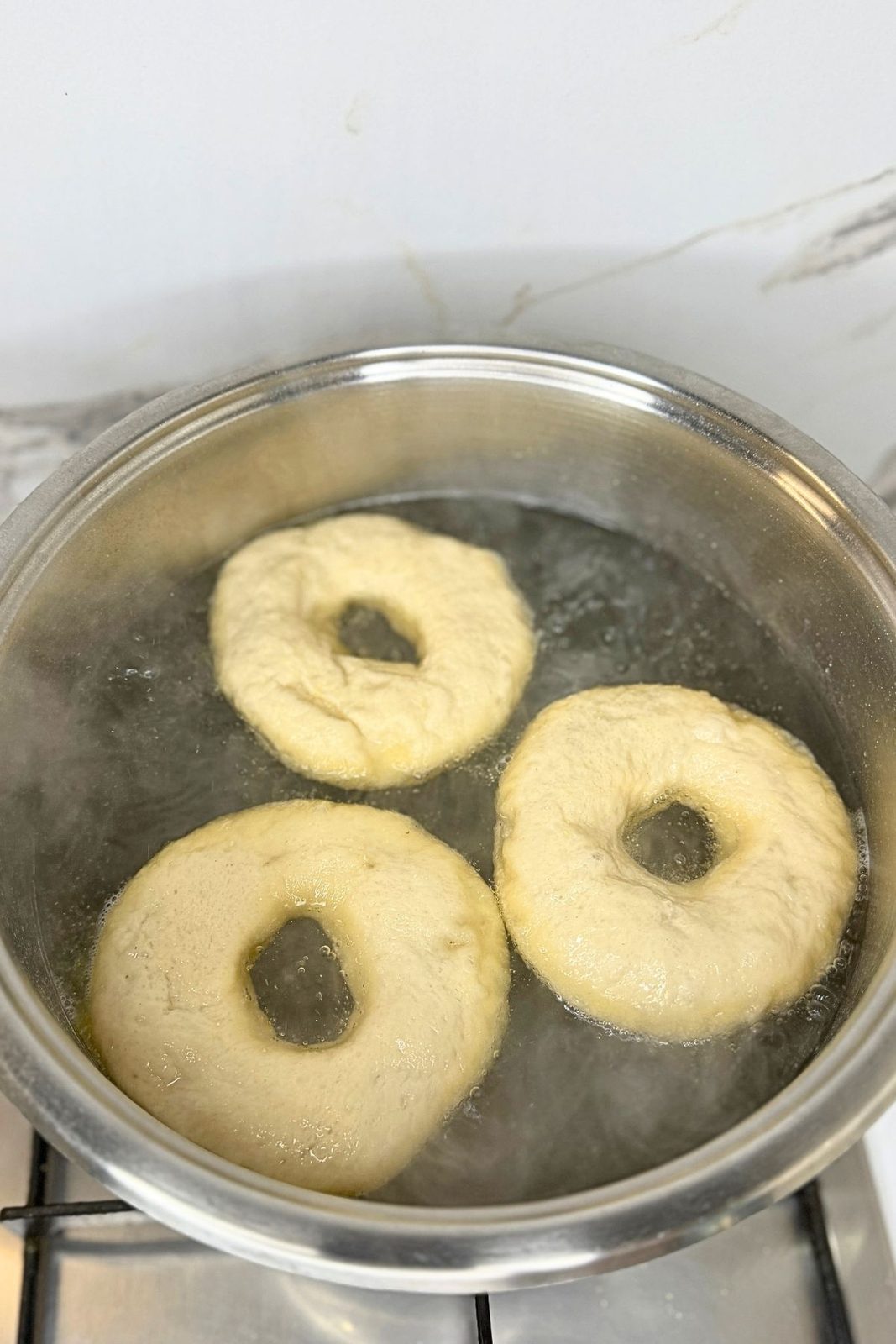 Three homemade bagels boiling in a large pot of water with baking soda and honey.