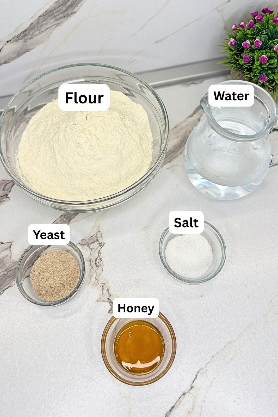 Ingredients for homemade bagels in labeled containers, including flour, water, dry yeast, salt, and honey.