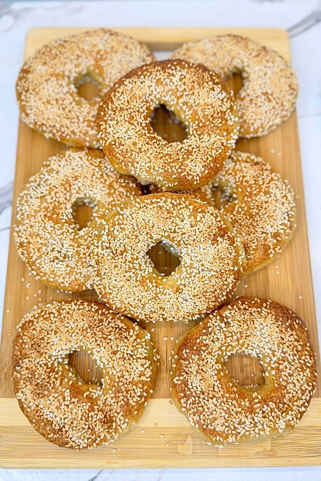 Golden homemade bagels covered with toasted sesame seeds and arranged on a wooden board.