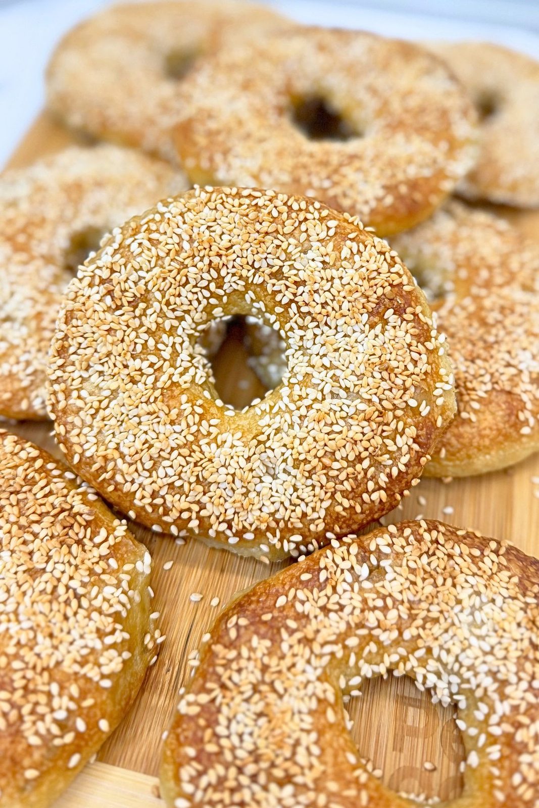 Close-up of golden homemade bagels topped with toasted sesame seeds on a wooden board.