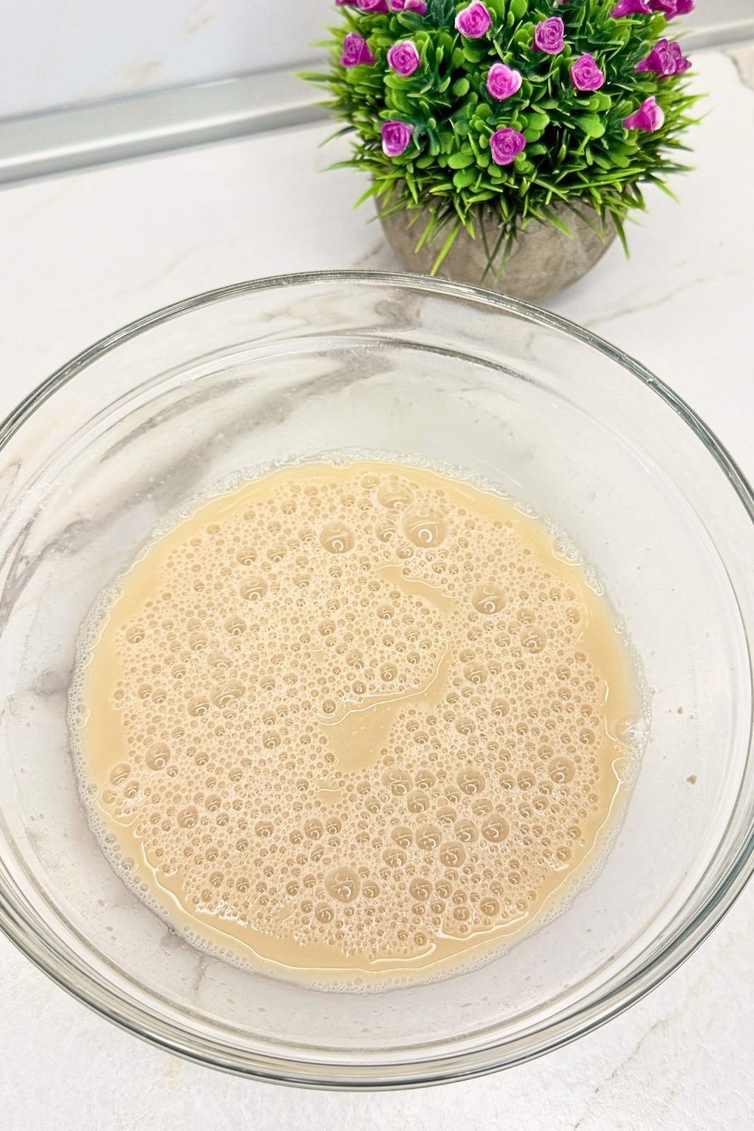 Foamy yeast mixture with lukewarm water and honey in a glass bowl for homemade bagels.