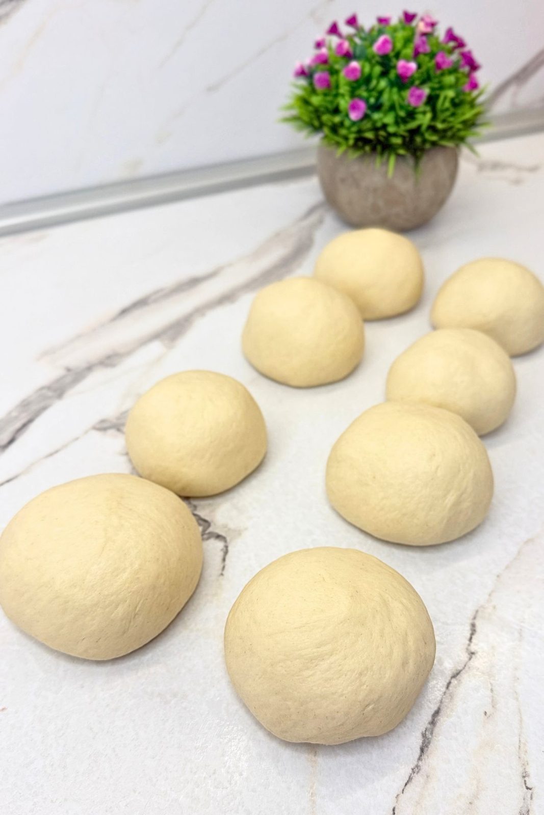Eight smooth balls of bagel dough resting on a marble work surface before shaping.