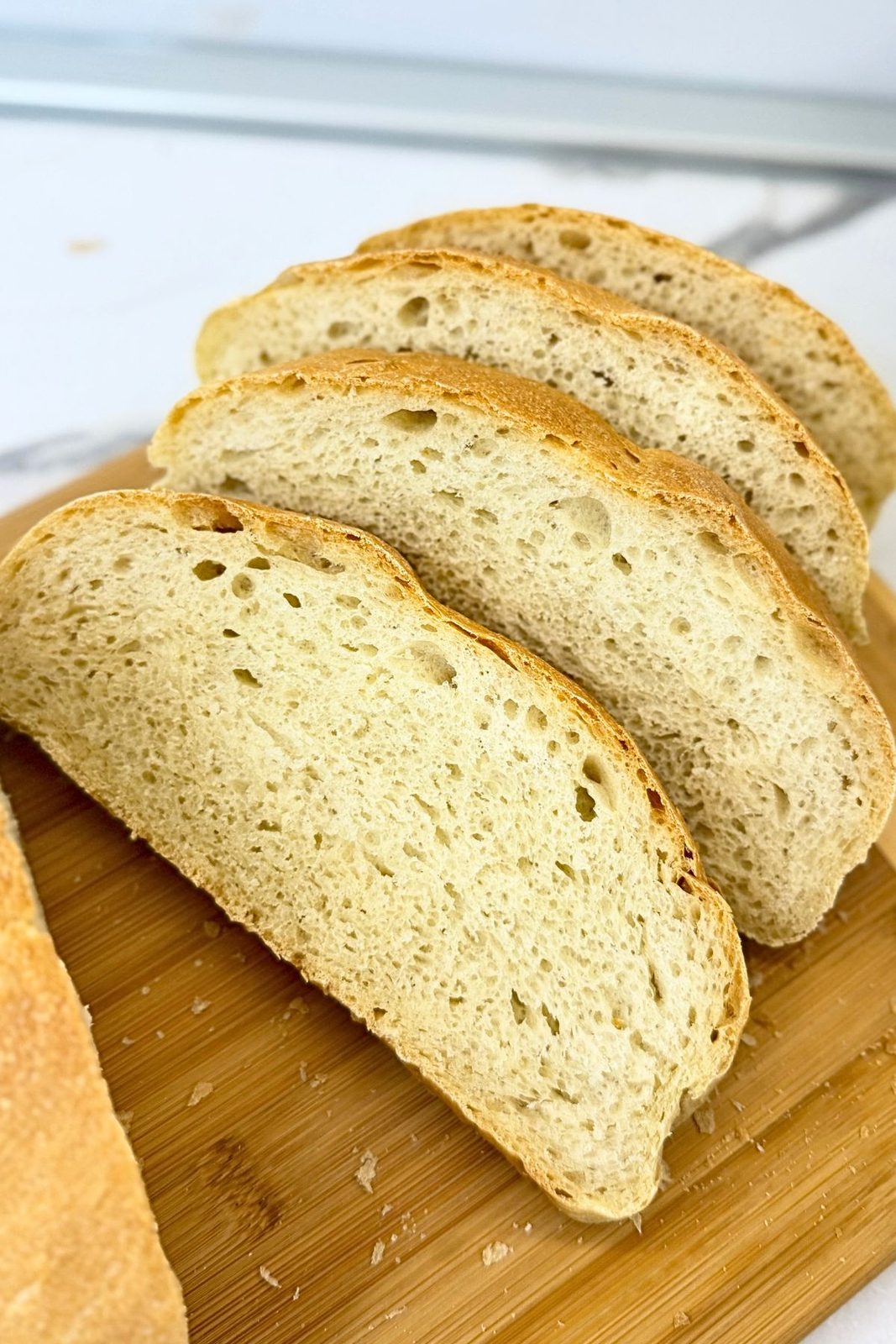 Homemade bread slices arranged on a wooden cutting board, showing a soft, airy crumb and thin golden crust.