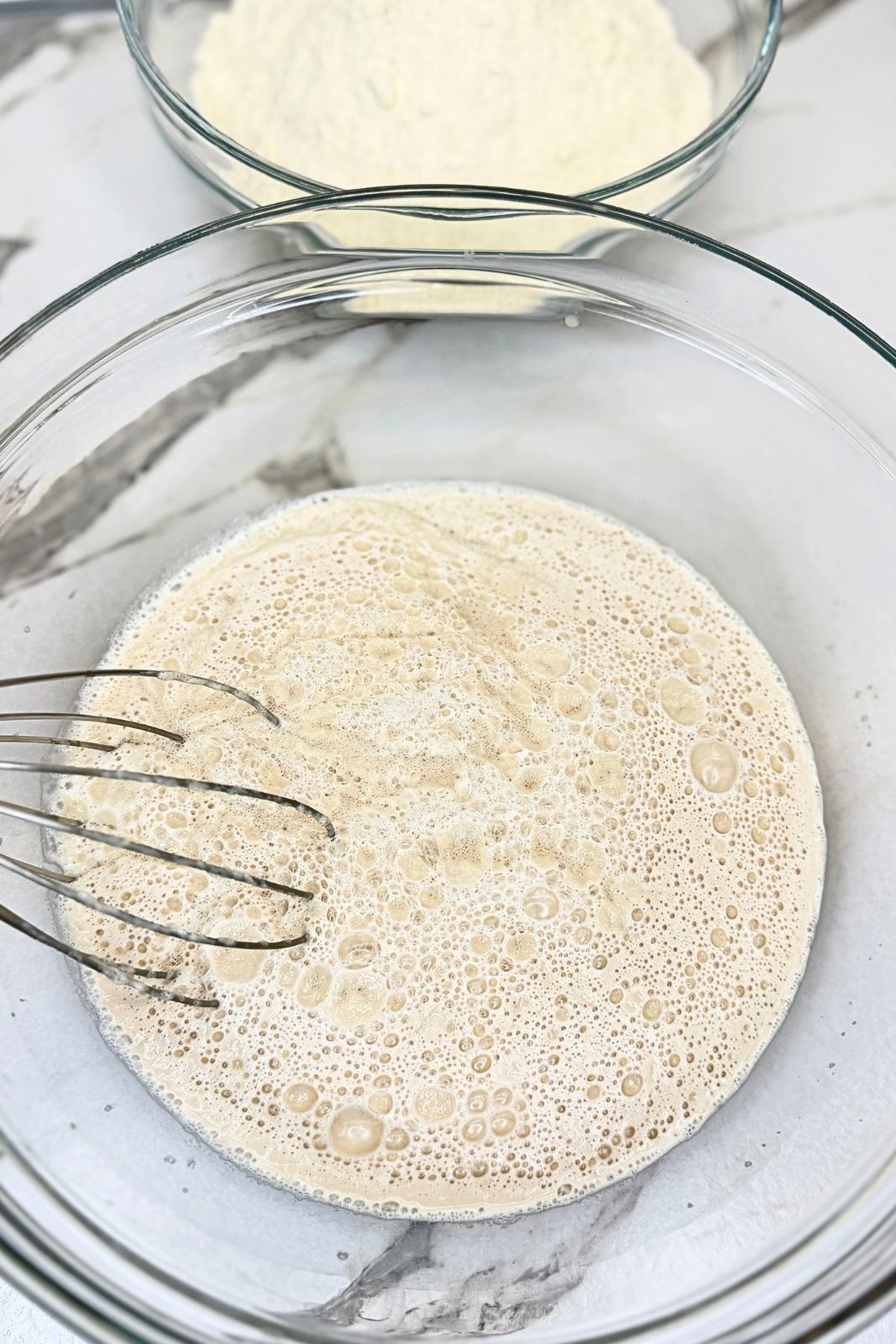 Foamy yeast mixture with warm water and honey in a glass mixing bowl.