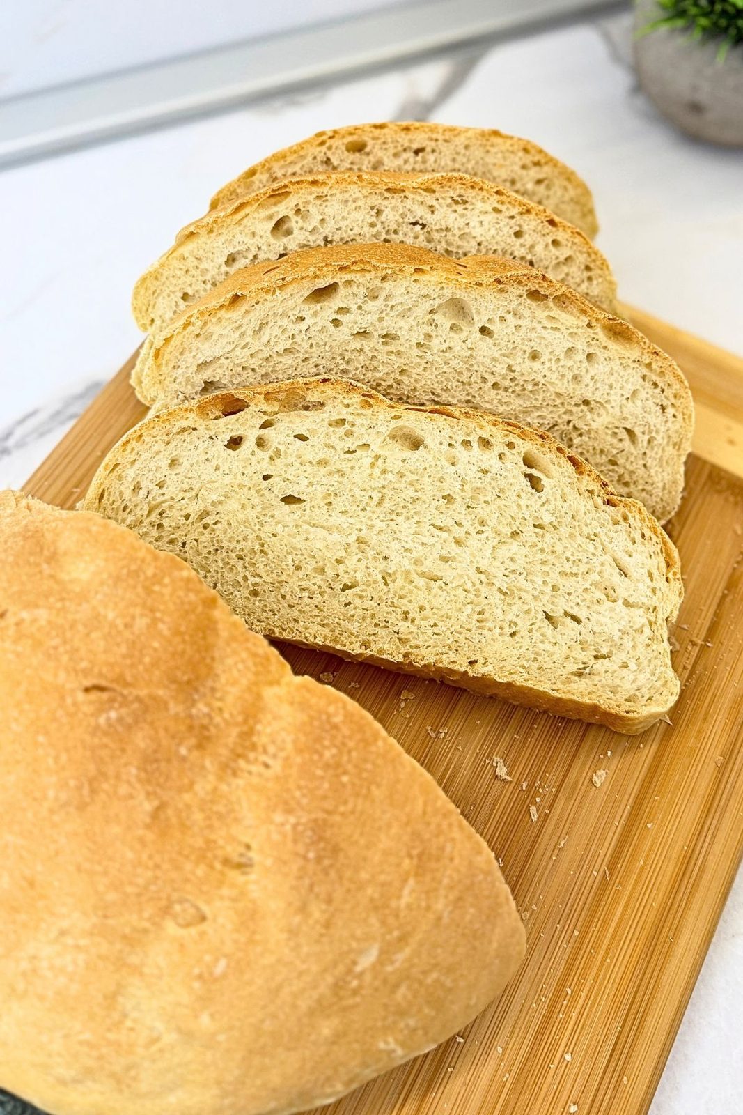 Homemade bread cut into thick slices, showing its airy interior on a wooden cutting board.