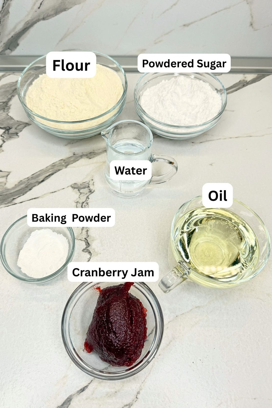 Ingredients for jam filled crescent cookies: all-purpose flour, powdered sugar, water, oil, baking powder, and cranberry jam in glass bowls and measuring cups.