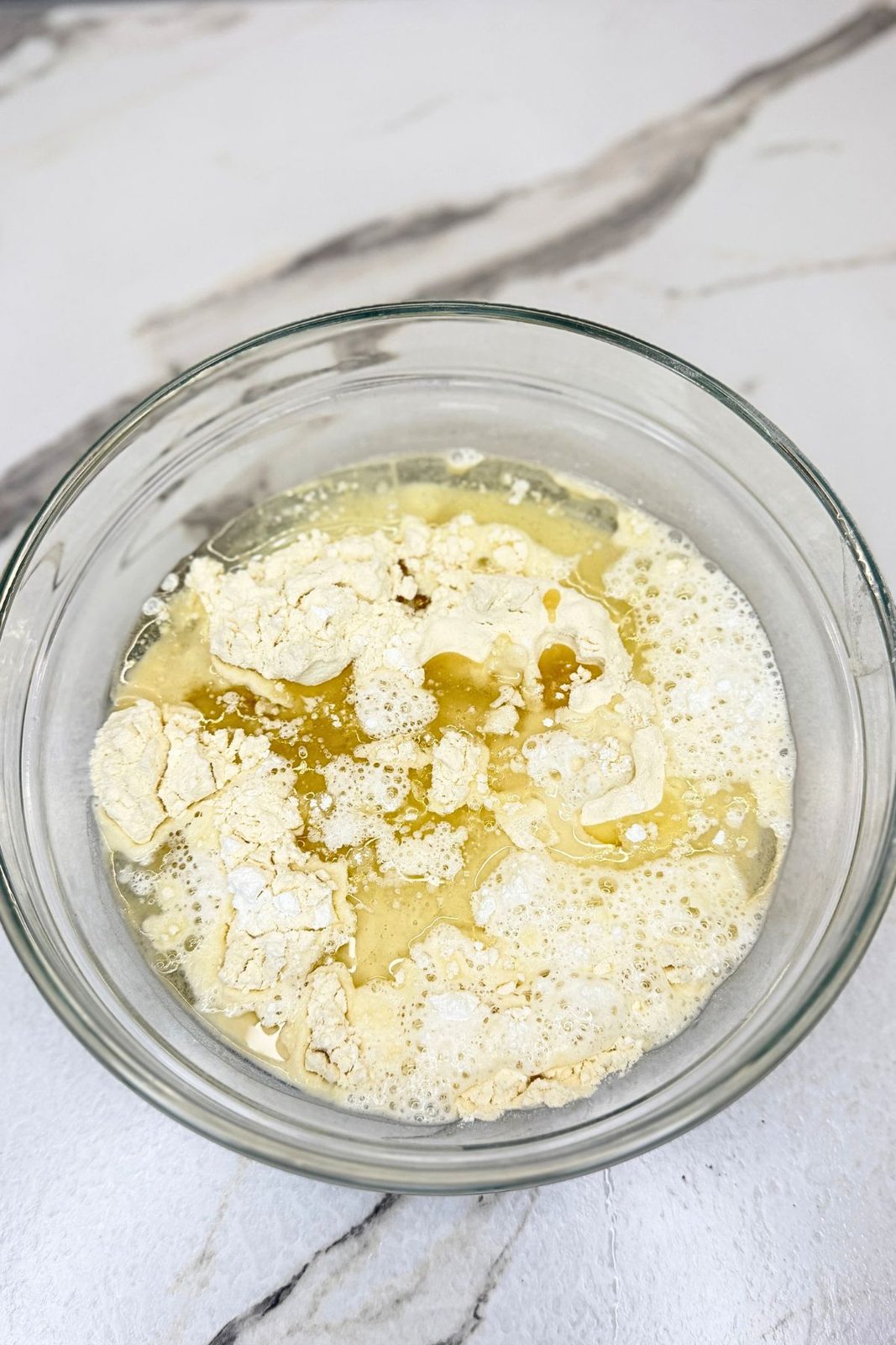 Flour, baking powder, oil, and hot water in a glass bowl before mixing the dough for jam filled crescent cookies.