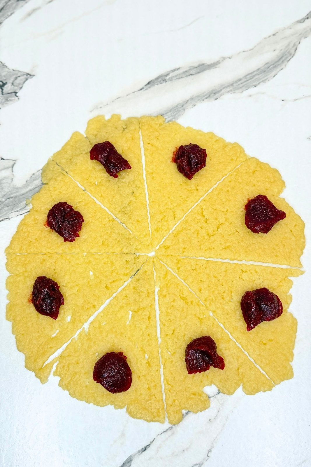 Rolled cookie dough cut into eight wedges, each topped with cranberry jam near the wide end.