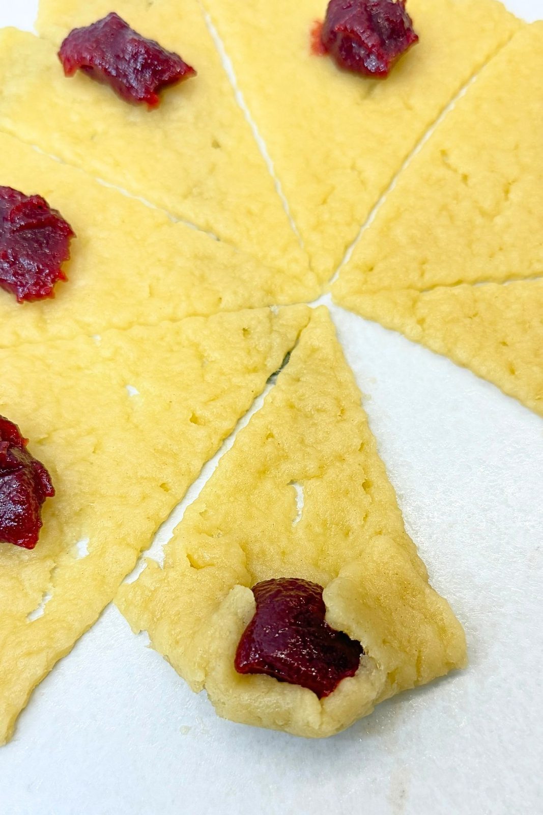 Rolling a dough wedge around cranberry jam to shape a jam filled crescent cookie.