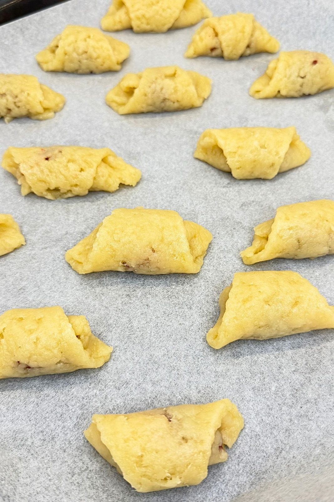 Unbaked jam filled crescent cookies arranged on a parchment-lined baking sheet.