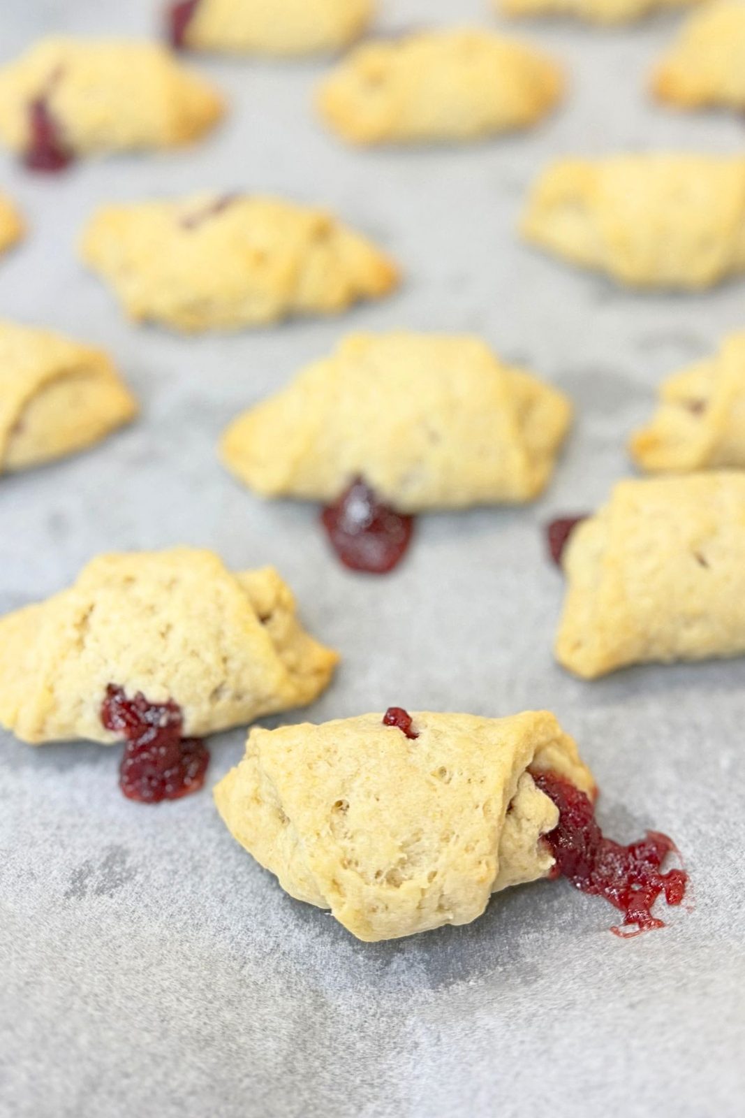 Baked jam filled crescent cookies with lightly golden edges and cranberry jam visible at the ends.