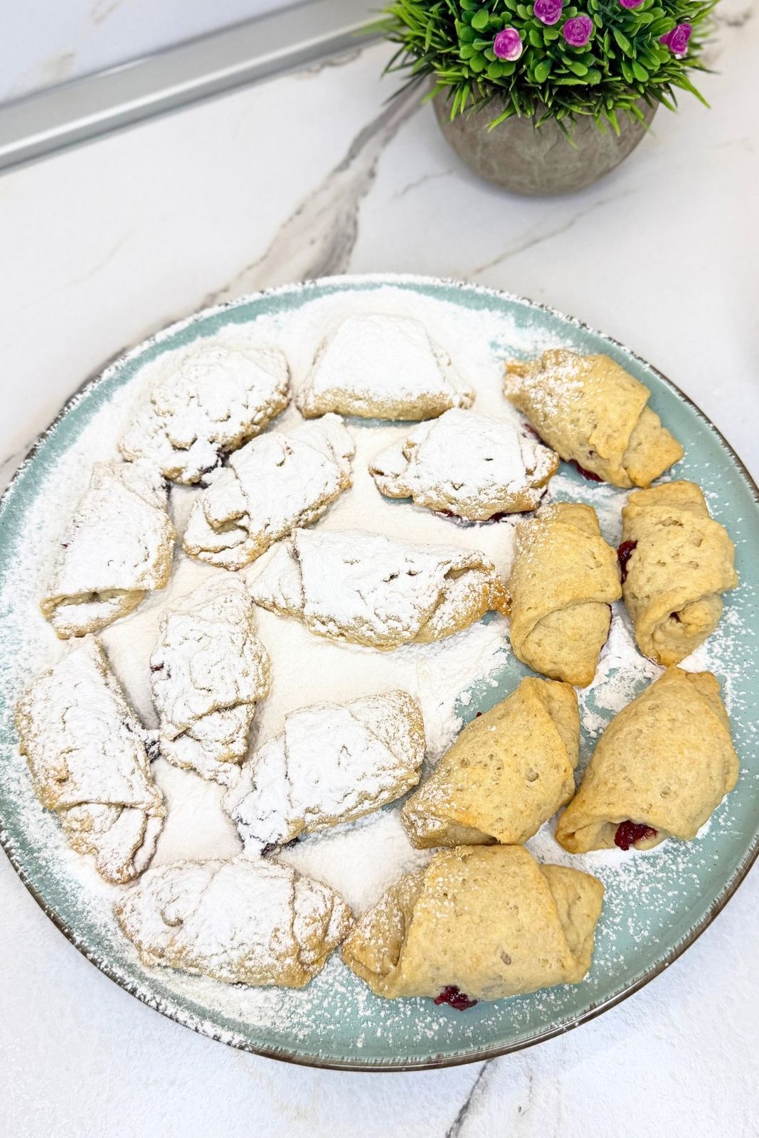 Jam filled crescent cookies on a pale green platter, some coated in powdered sugar and others still plain.