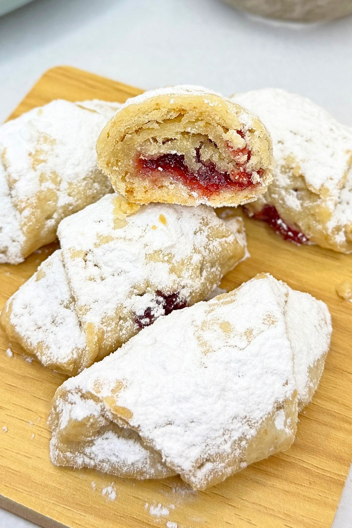Jam filled crescent cookies dusted with powdered sugar, with one cut open to reveal the cranberry jam filling.