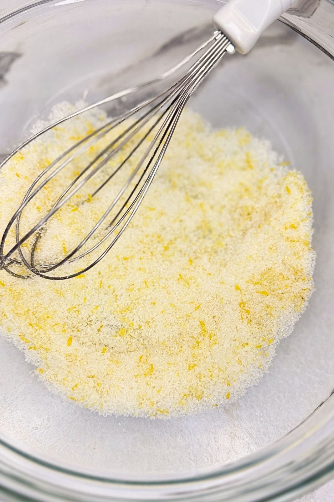 Sugar mixed with fresh lemon zest in a glass bowl with a whisk.