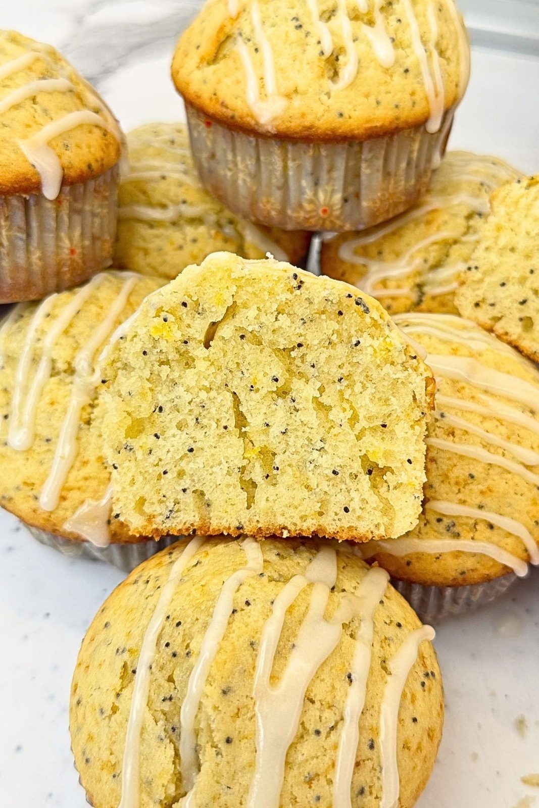 Golden lemon poppy seed muffins drizzled with lemon glaze, with a whole muffin in the center.