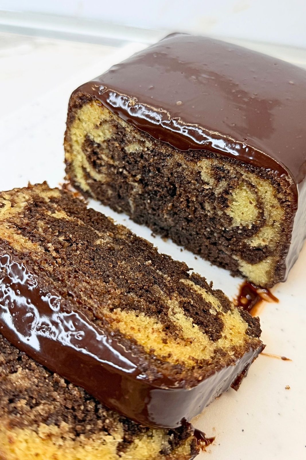 Marble loaf cake with one slice cut, revealing vanilla and chocolate swirls beneath a chocolate ganache topping.