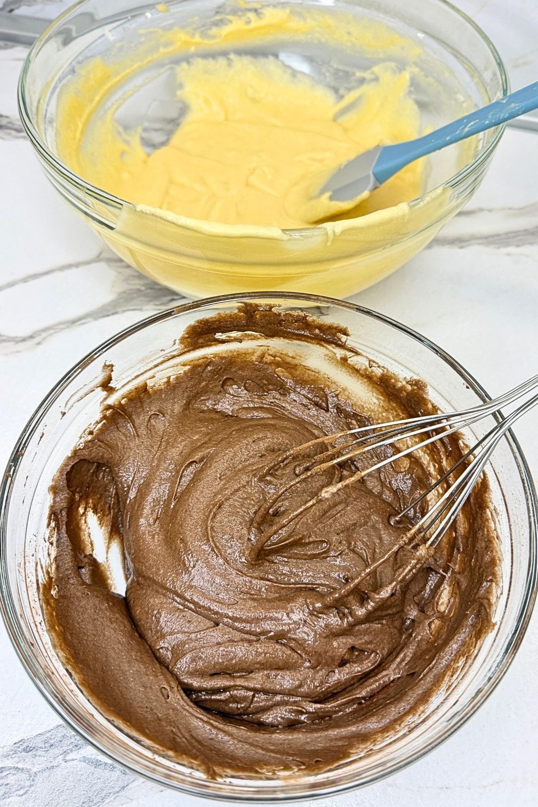 Chocolate and vanilla batters in separate glass bowls, ready to layer in a loaf pan.