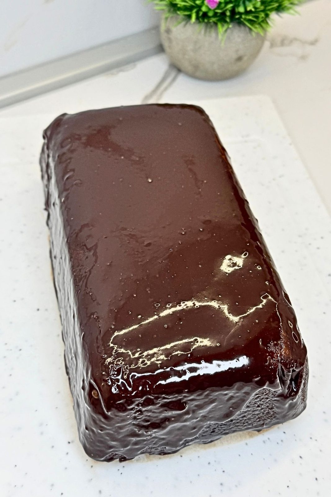 Whole marble loaf cake covered with glossy chocolate ganache on a white serving board.