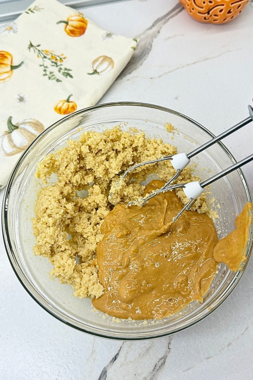 Creamy peanut butter added to creamed butter and sugars in a glass mixing bowl with a hand mixer.