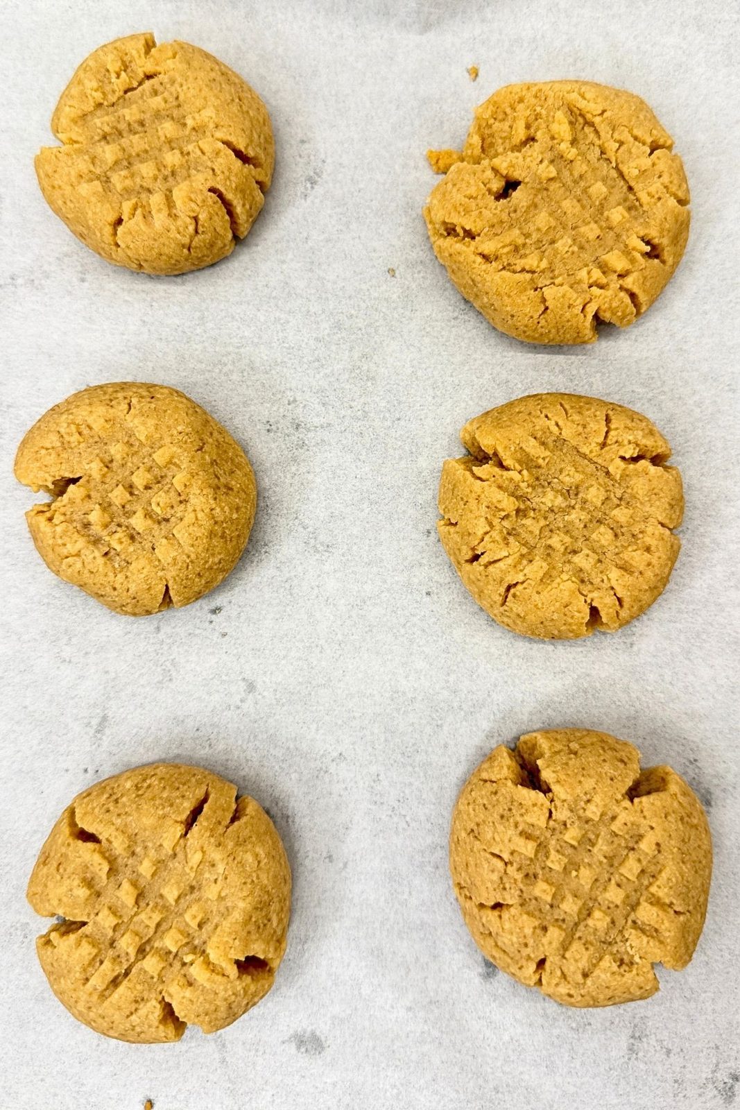 Freshly baked peanut butter cookies with golden edges and crisscross fork marks cooling on a parchment-lined baking sheet.
