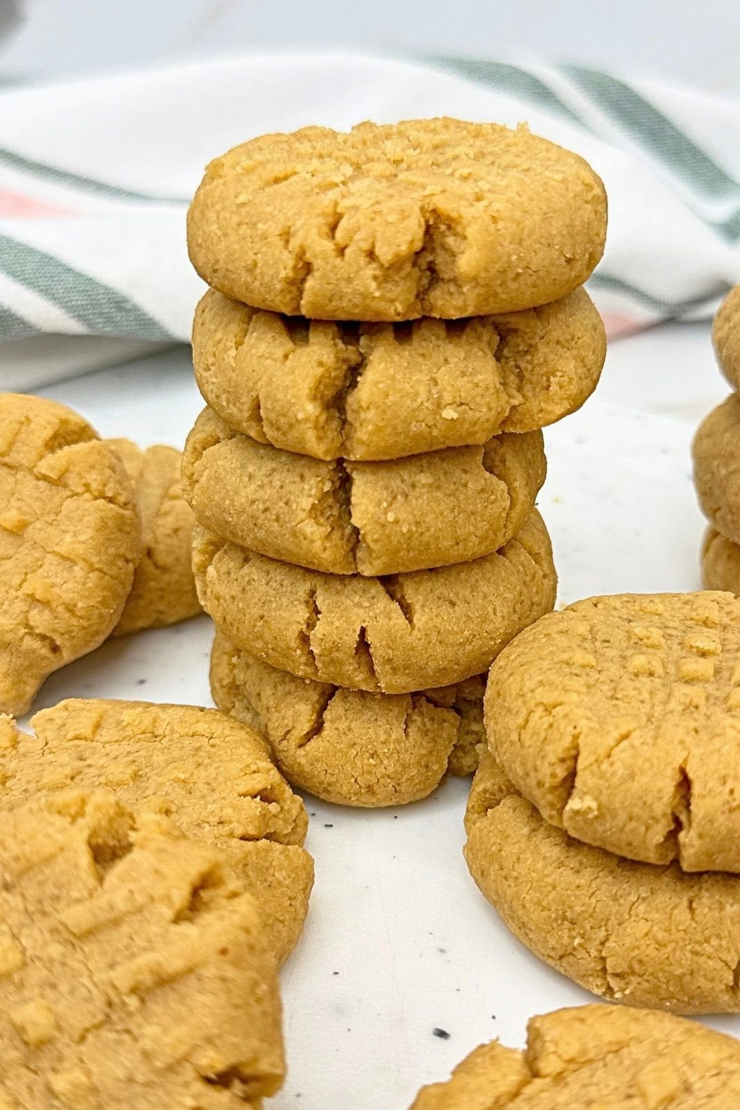 Stack of five peanut butter cookies with golden cracked edges and crisscross fork marks on a white surface.