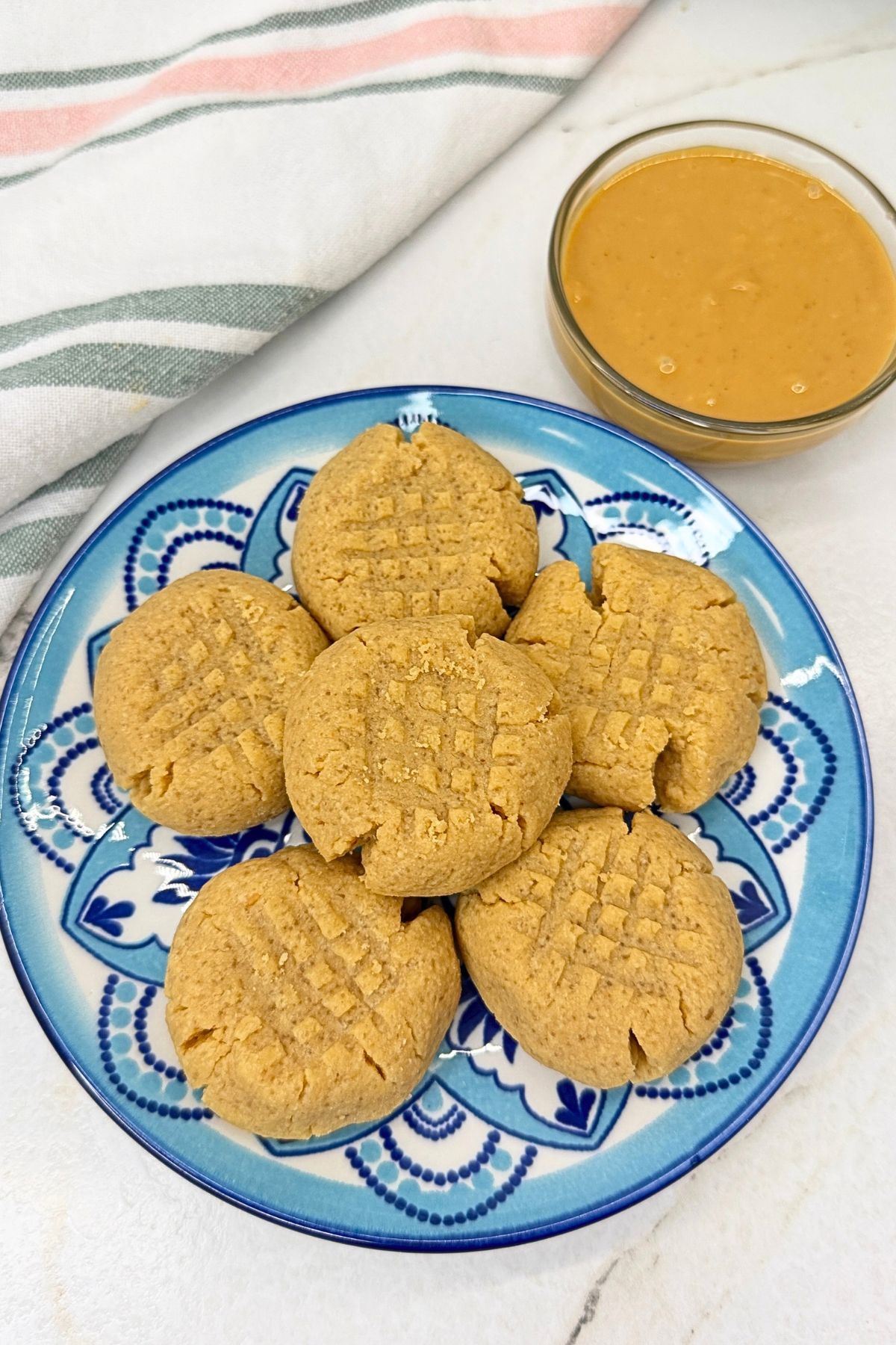 Peanut butter cookies with classic crisscross fork marks on a white platter beside a bowl of creamy peanut butter.