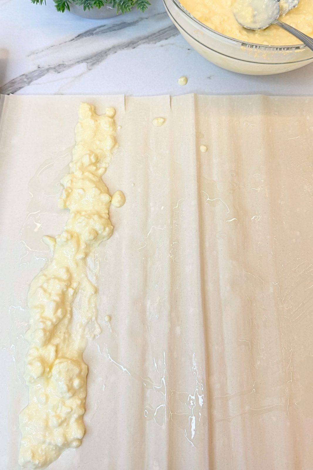 A line of creamy cheese filling spooned along the edge of an oiled phyllo sheet before rolling.