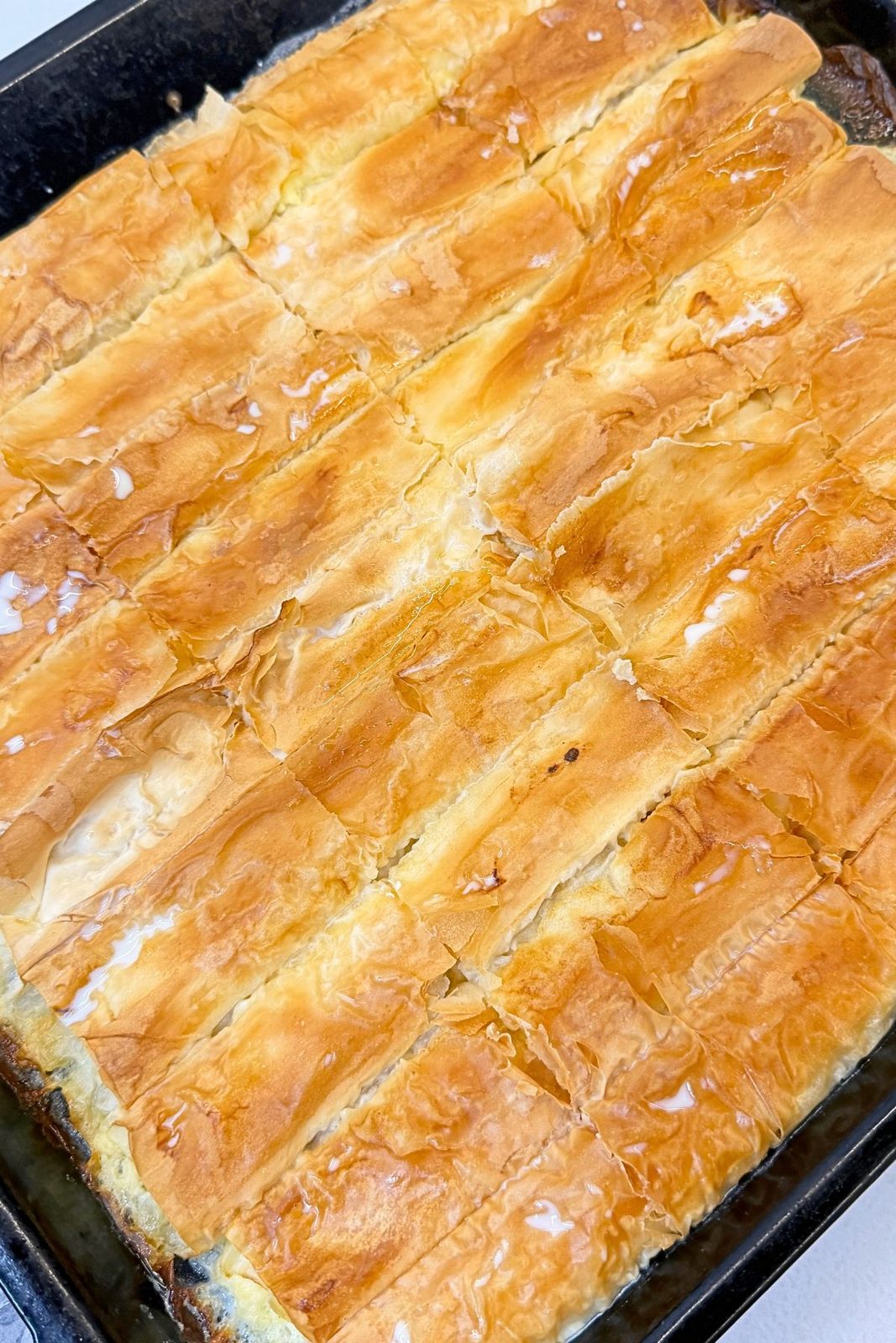 Golden phyllo cheese rolls brushed with milk after baking, resting in the pan before slicing.