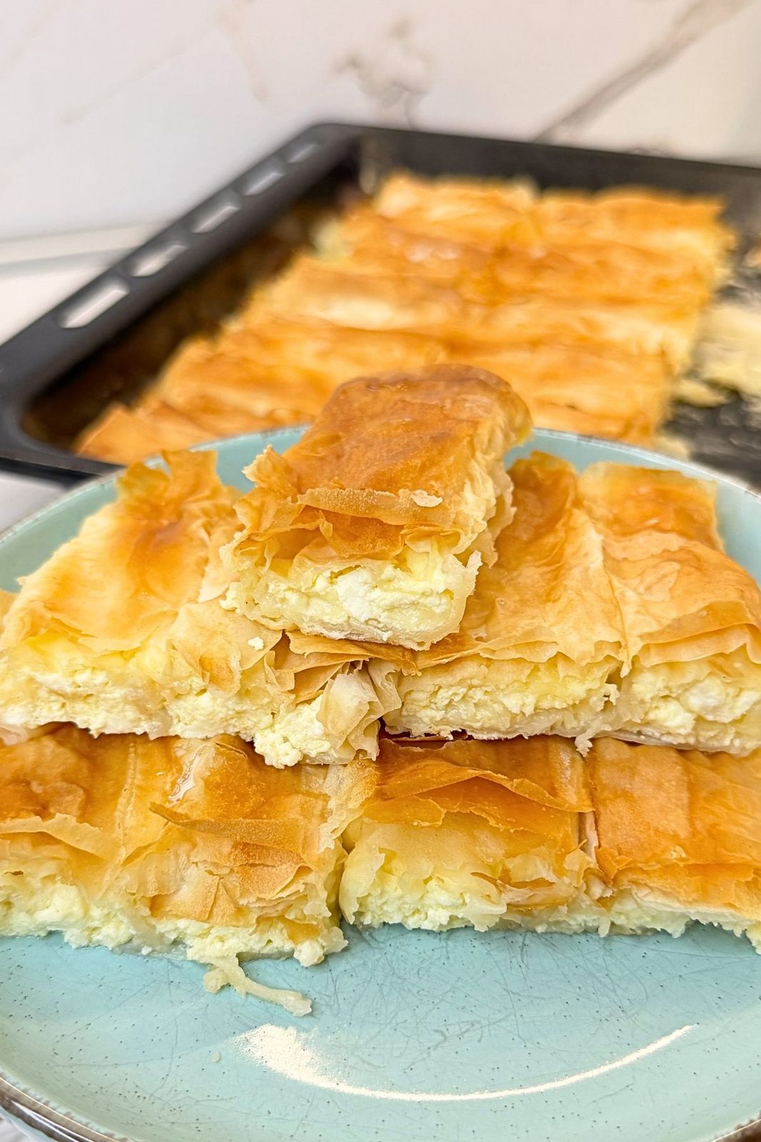 Golden phyllo cheese rolls on a turquoise plate, with a cut piece on top showing the creamy cottage cheese filling.