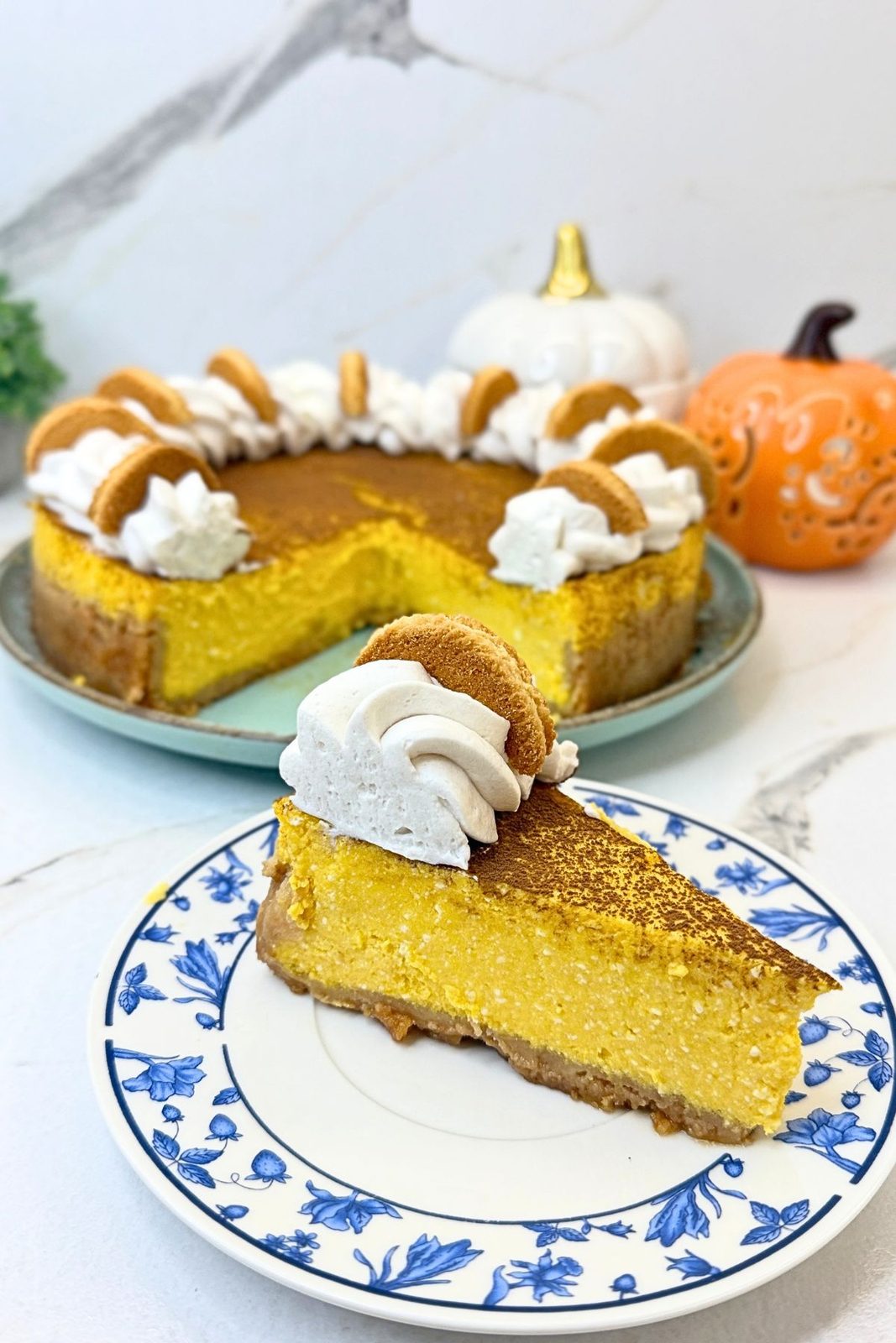 Slice of pumpkin cheesecake with a graham cracker crust and whipped cream on a blue-and-white plate.