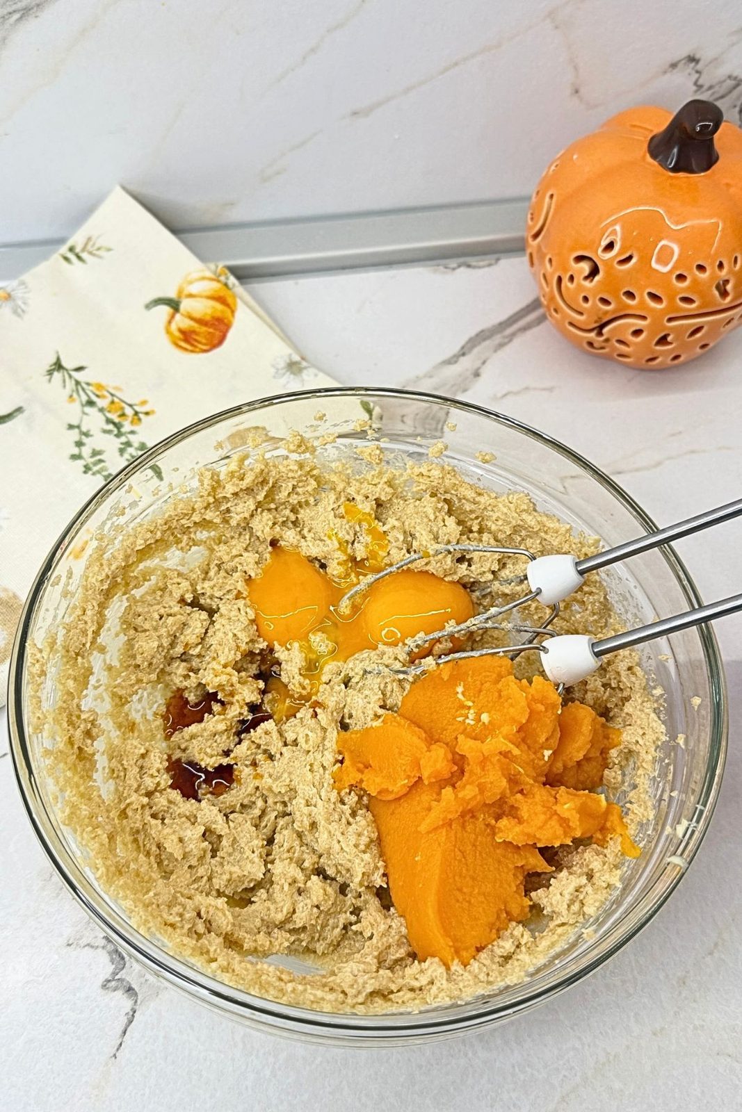 Pumpkin purée, egg yolks, and vanilla added to creamed butter and brown sugar in a glass mixing bowl for pumpkin cookies.
