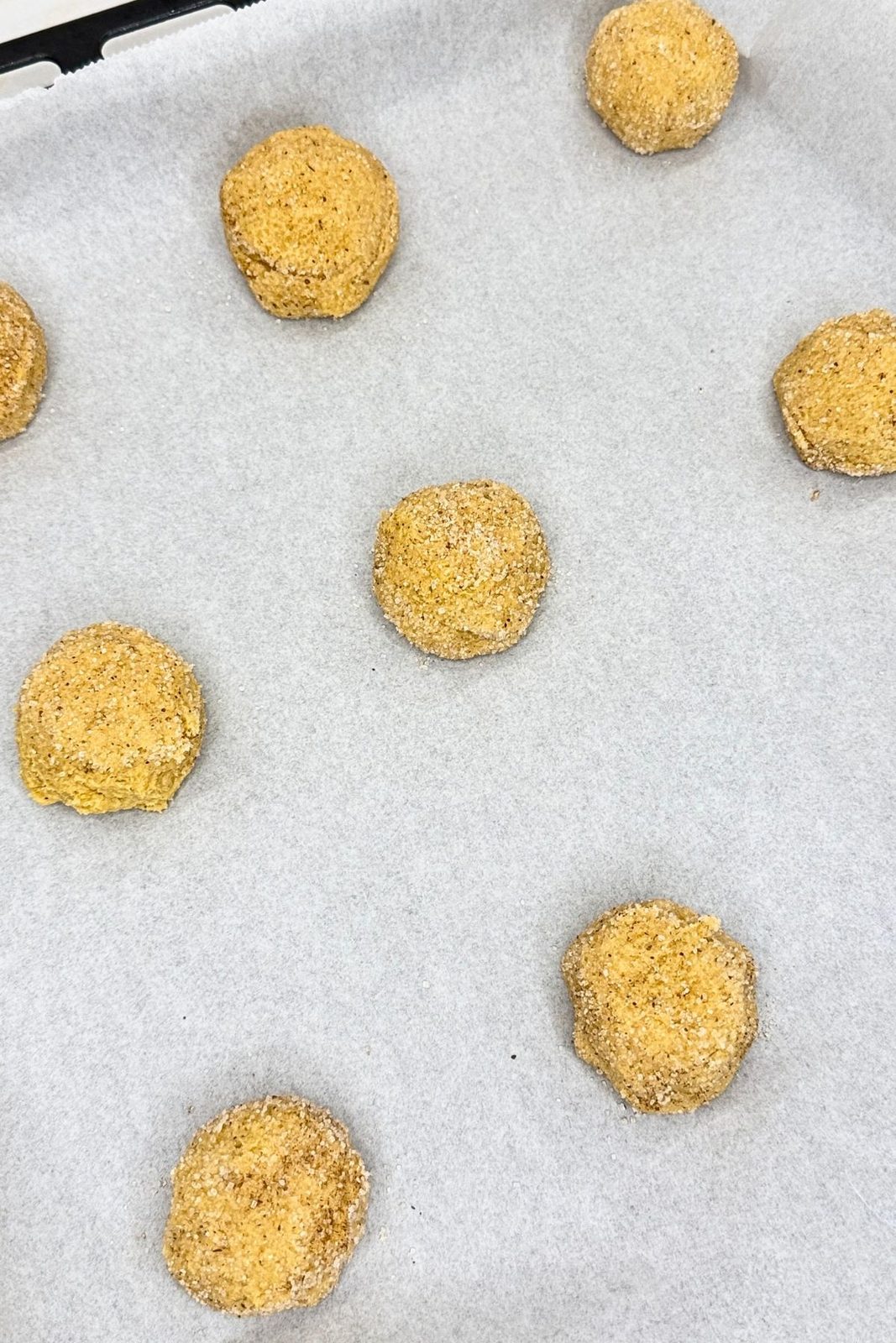 Pumpkin cookie dough balls coated in spiced sugar and spaced apart on a parchment-lined baking sheet.

