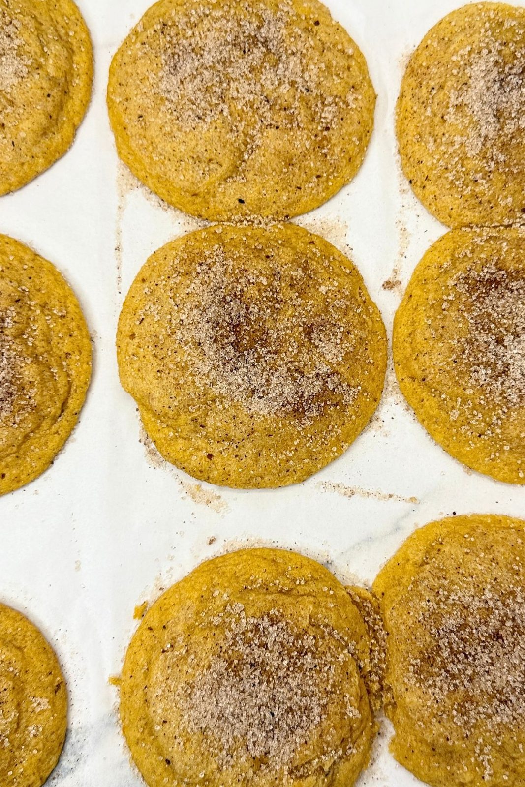 Freshly baked pumpkin cookies with spiced sugar tops cooling on parchment paper.
