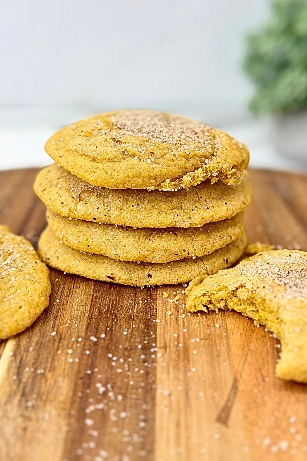Pumpkin cookies coated in spiced sugar stacked on a wooden board, with a broken cookie beside them showing the soft center.
