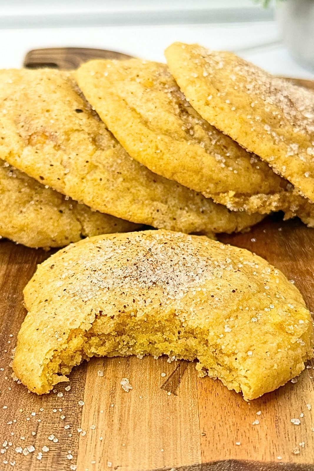 Pumpkin cookies on a wooden board, with a broken cookie in the foreground showing its soft center and spiced sugar coating.
