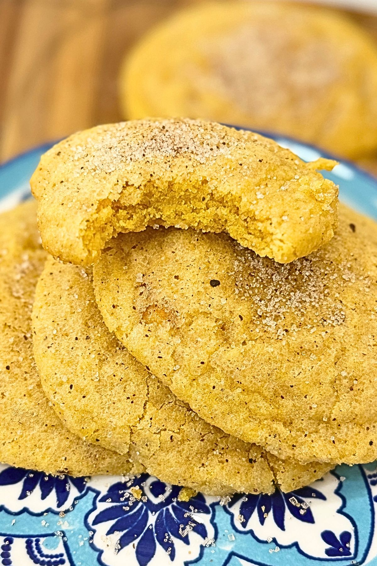 Chewy pumpkin cookies coated in spiced sugar on a ceramic plate, with a broken cookie on top showing the soft center.
