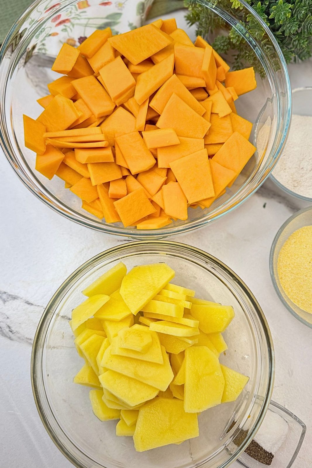 Thinly sliced pumpkin and potatoes in separate glass bowls, ready to coat.