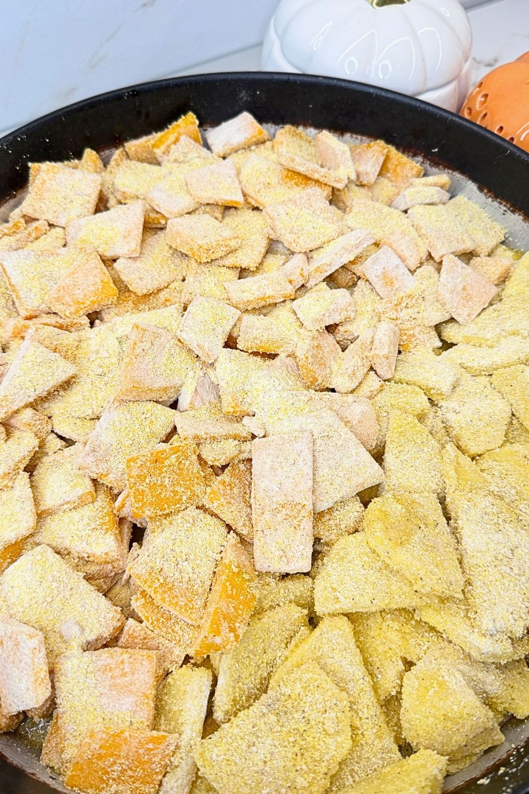 Cornmeal and buckwheat flour coated pumpkin and potatoes arranged on opposite sides of a round baking pan.