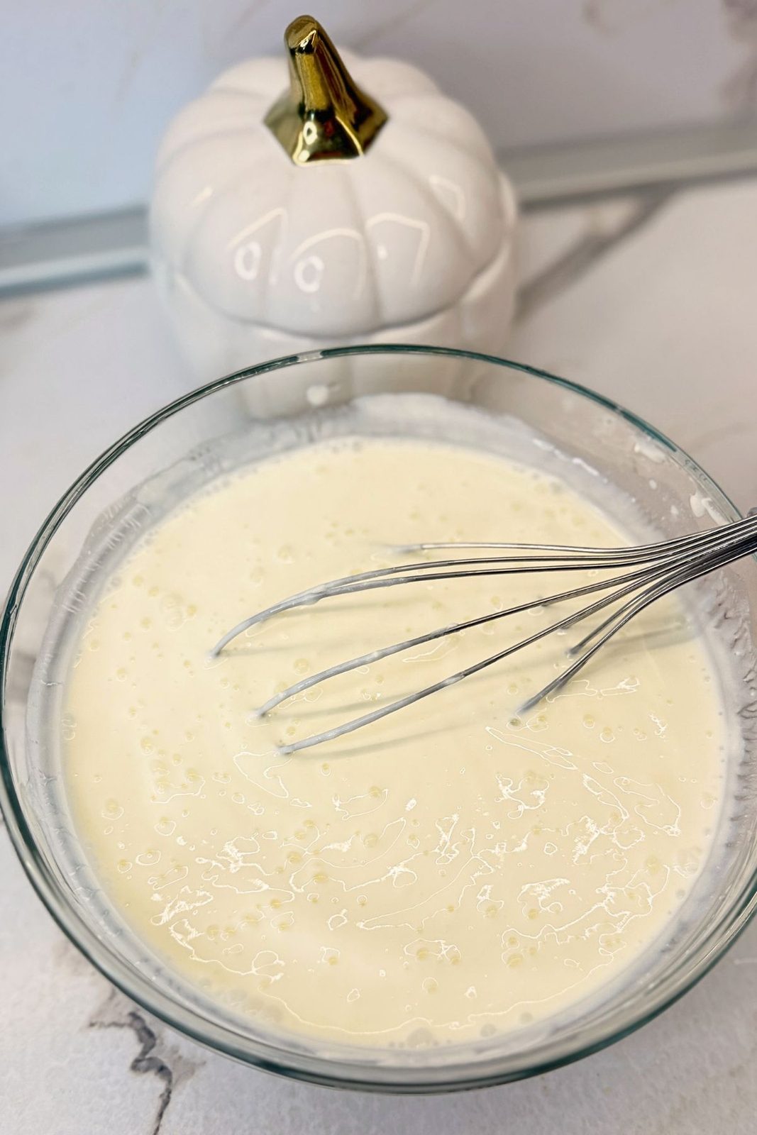 Creamy garlic yogurt and sour cream sauce mixed in a glass bowl with a whisk.