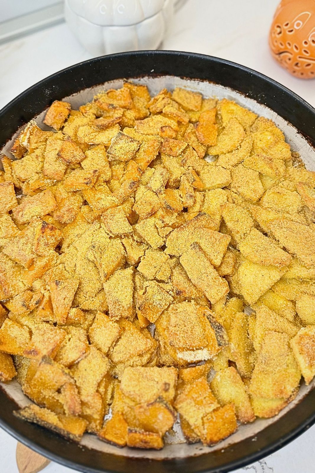Roasted pumpkin and potatoes with golden edges and a cornmeal coating in a round baking pan.