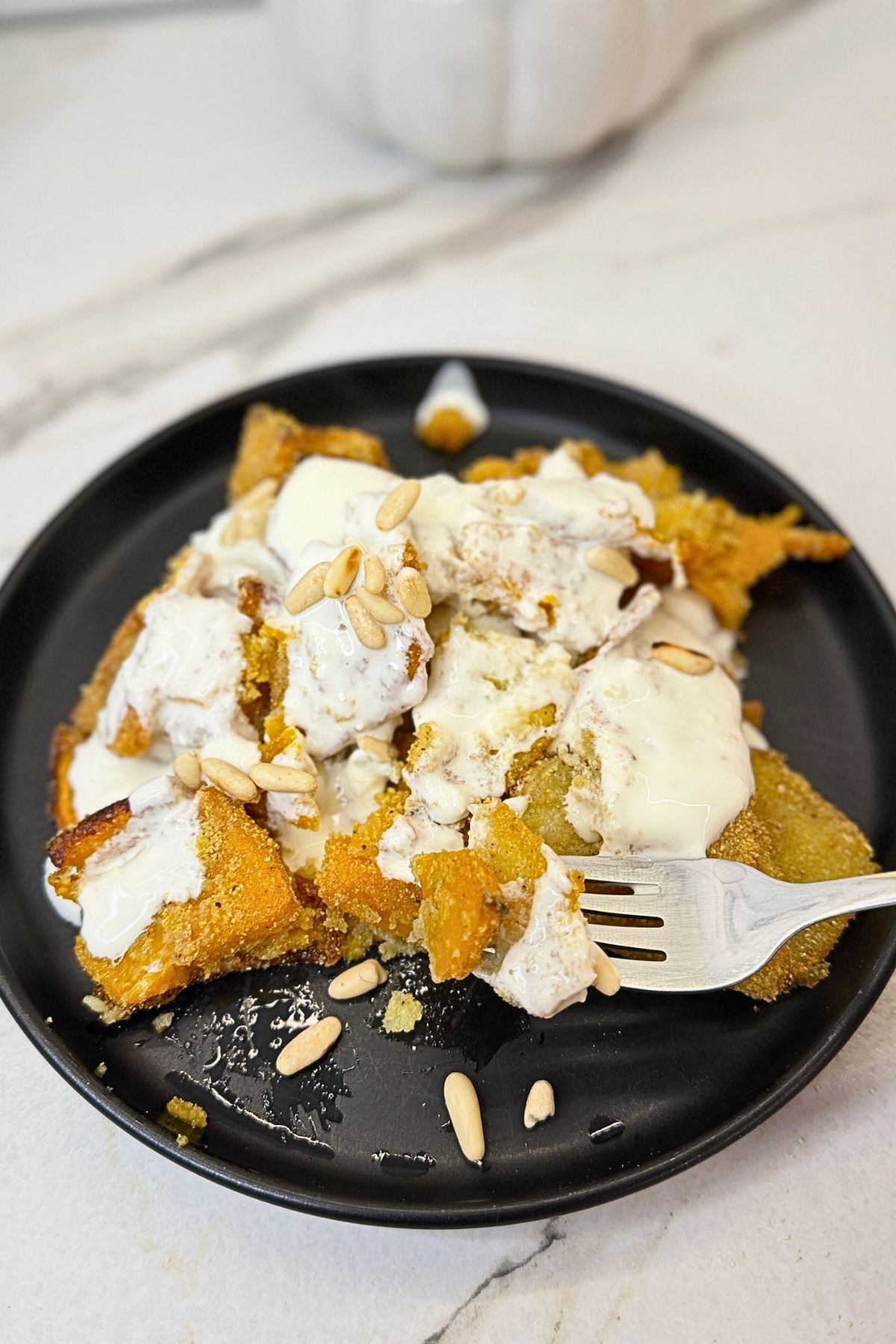 Roasted pumpkin and potatoes topped with creamy garlic yogurt sauce and pine nuts on a ceramic plate.