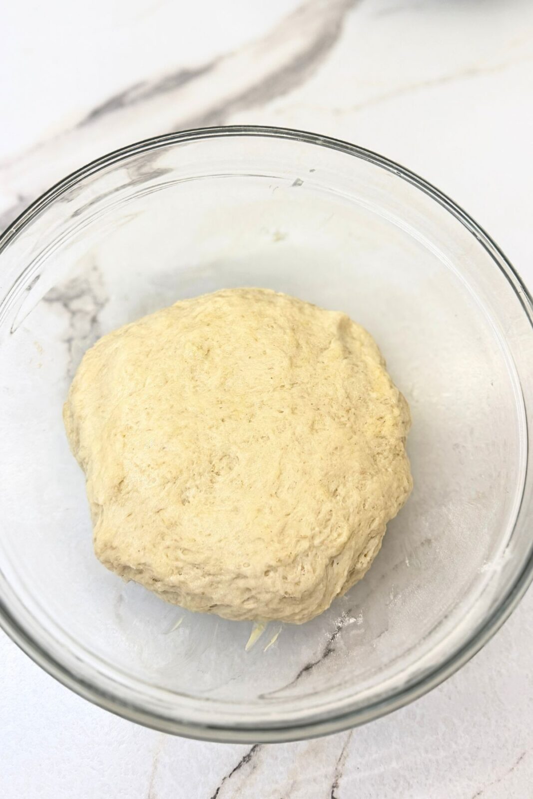 Homemade crescent roll dough gathered into a ball in a glass mixing bowl.