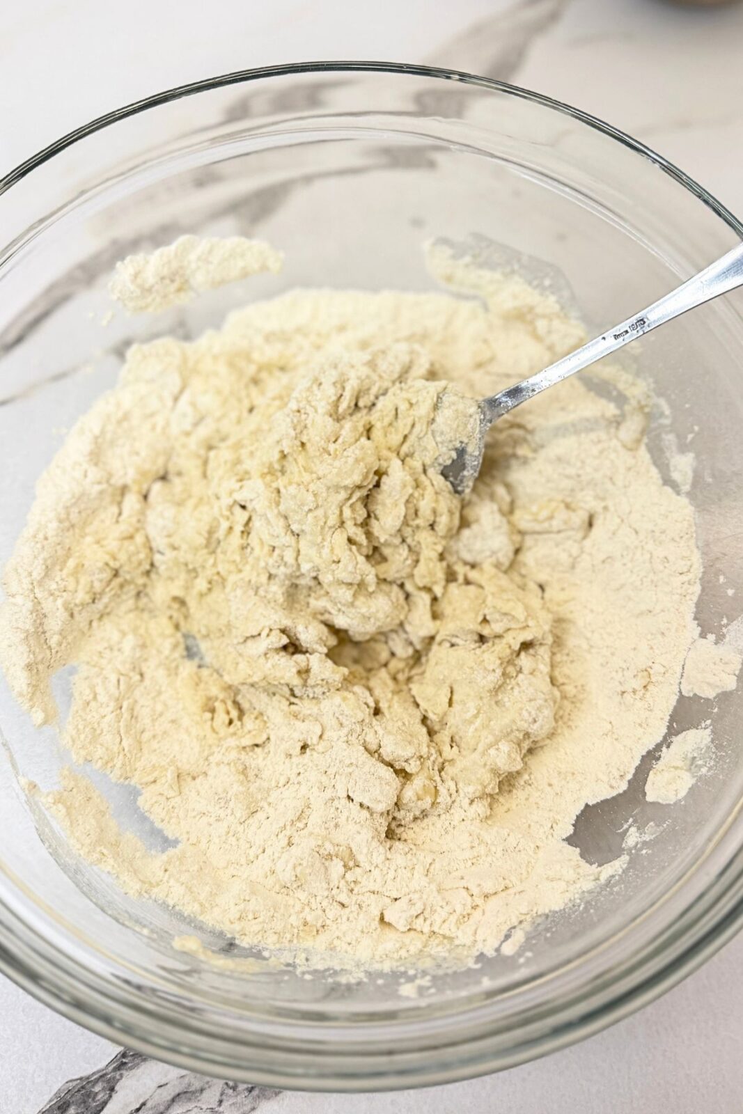 Flour and wet ingredients partially mixed with a spoon in a glass bowl to make homemade crescent roll dough.