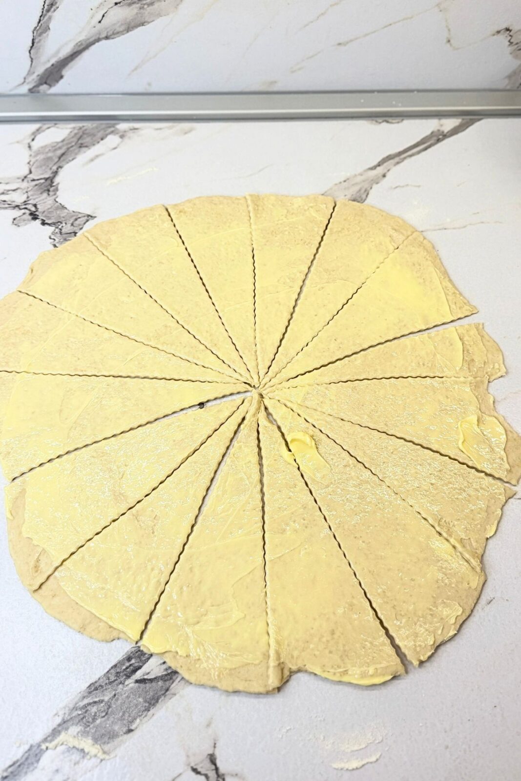 Rolled-out crescent roll dough cut into 16 triangular wedges on a lightly floured countertop.