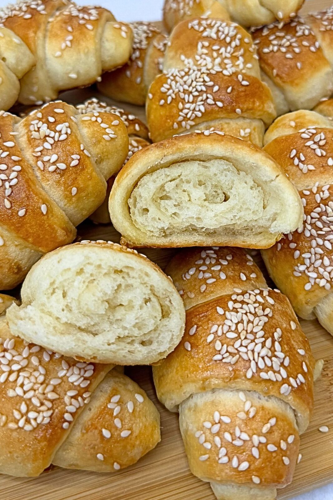 Close-up of golden homemade crescent rolls topped with sesame seeds, with two cut halves showing the soft interior and rolled layers.