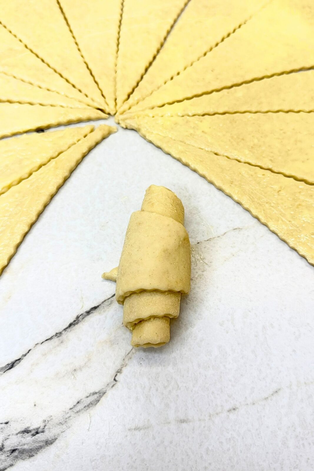 A shaped crescent roll beside triangular dough wedges on a lightly floured countertop.